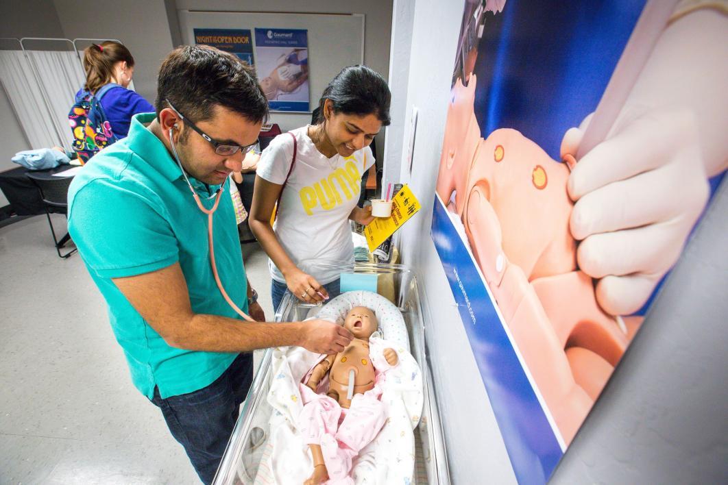 A man and a woman use a stethoscope on an infant medical dummy.