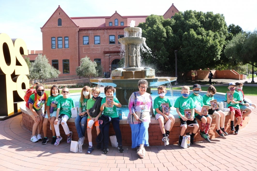 group of youn students seated with an older woman in front of a fountain