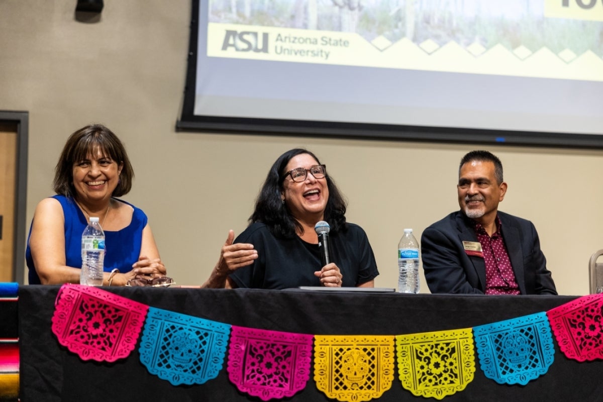 Woman speaking into a microphone while other panelists look on, smiling. 