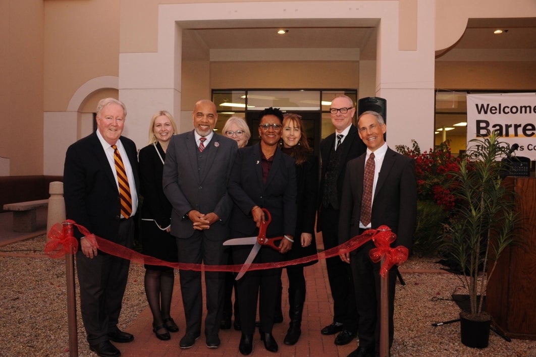 A group of people stand behind a ribbon at a ribbon-cutting.