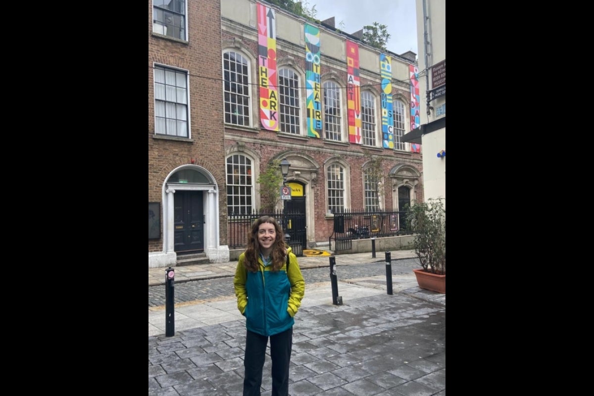 Person standing on a city street in front of a line of buildings.