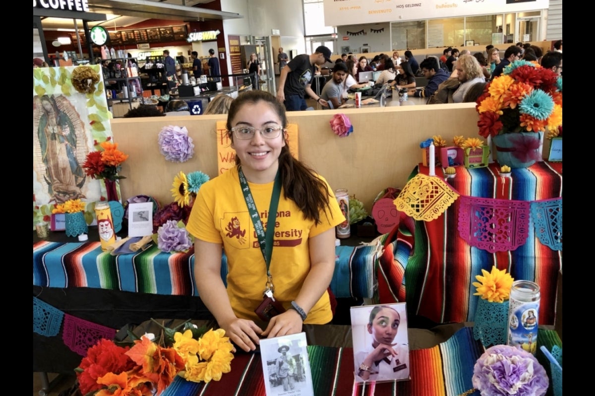 ASU CAMP scholar standing at a table with Dia de los Muertos gift items