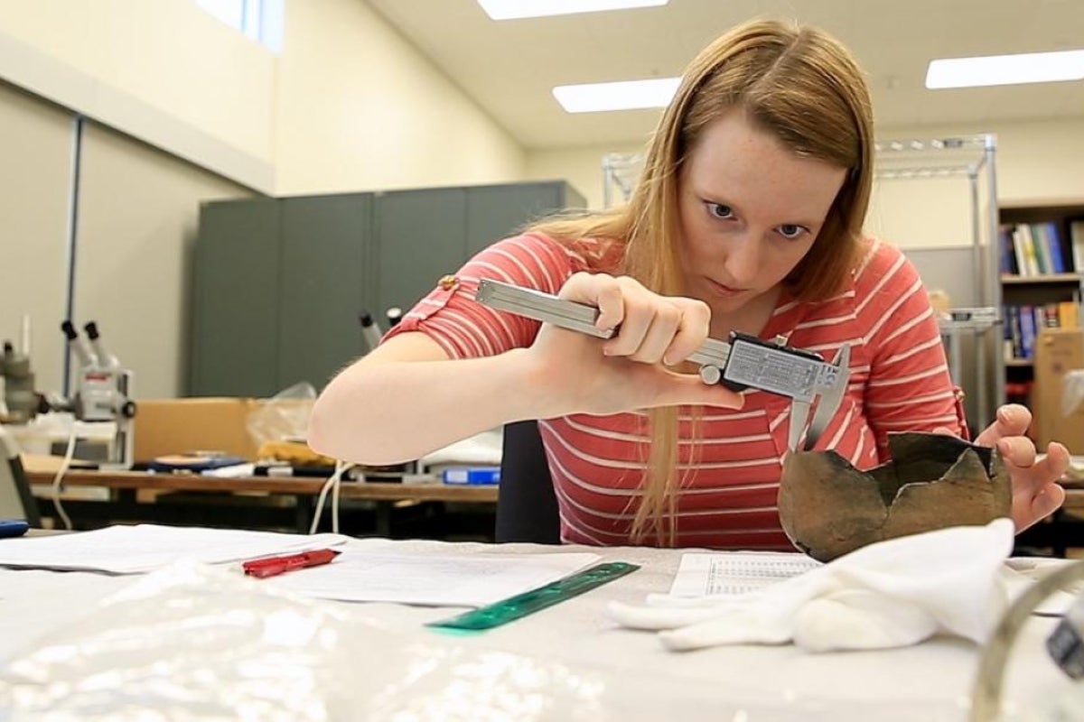 A student takes a measurement on an ancient pot.