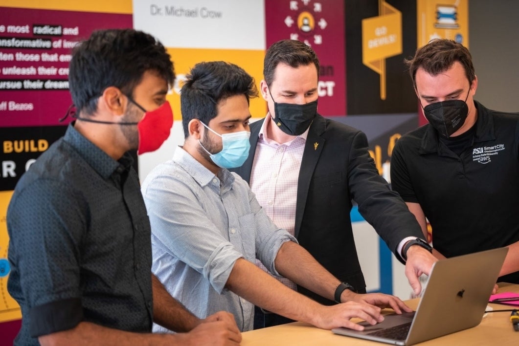 Ryan Hendrix, General Manager of the ASU Smart City Cloud Innovation Center (CIC), gathers with students around a laptop at the CIC.