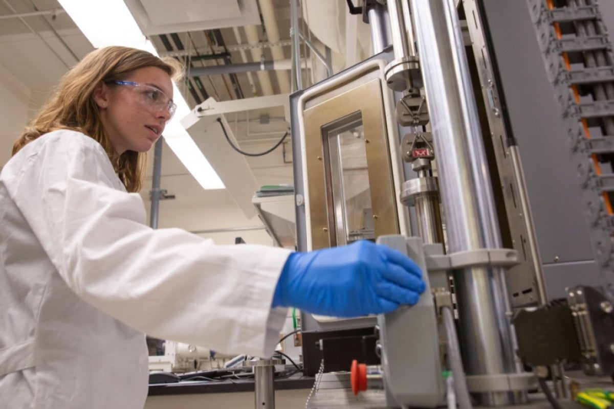 ASU alumna Alexis Hocken wearing a white lab coat, goggles and gloves in a lab. undergraduate student.