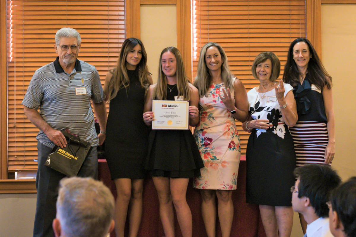 Group of people posing for a photo. The person in the middle holds up a certificate for a scholarship.