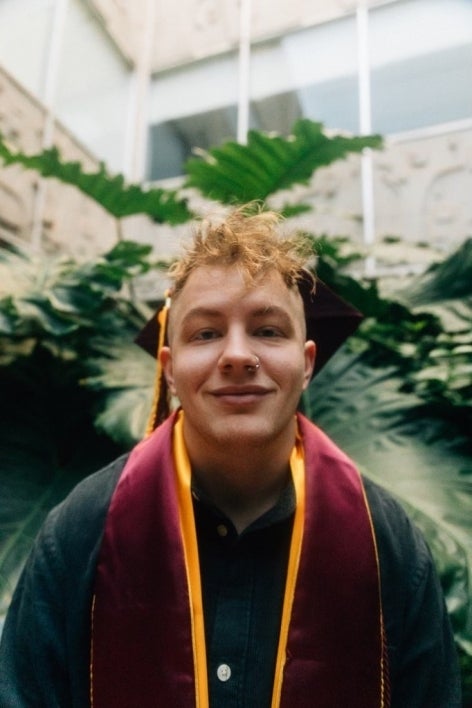 man wearing cap and gown with foliage in background