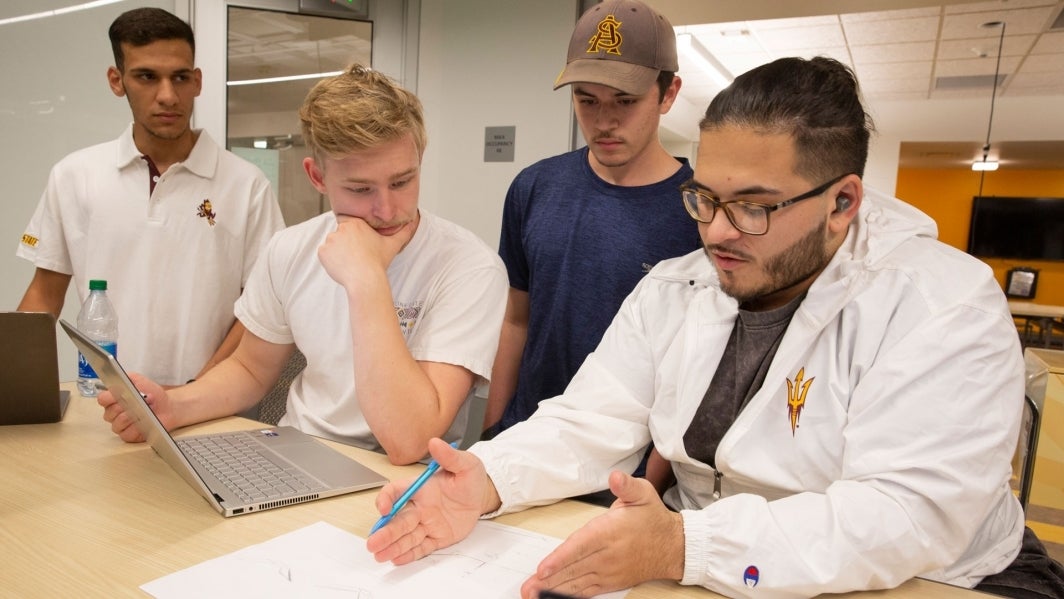 ASU students and members of Solar Devils gathered around a conference table, talking and looking at papers.