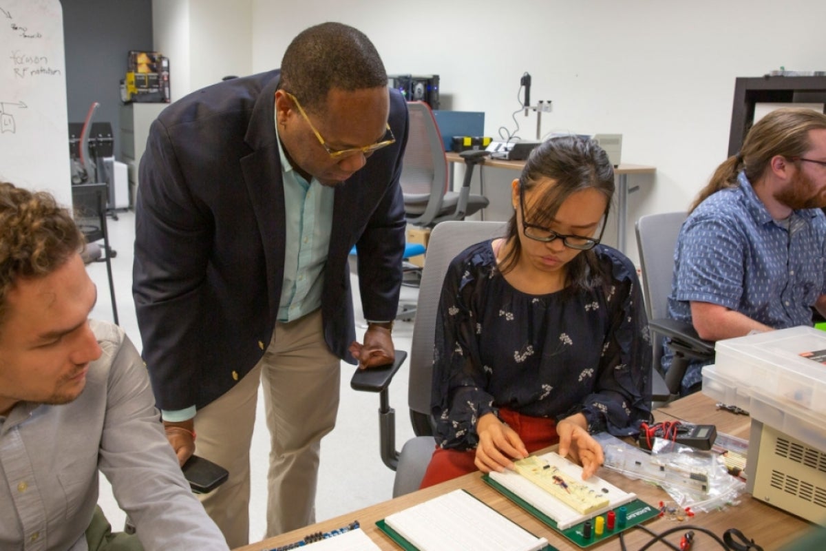 Michel Kinsy leans over to inspect hardware graduate students in the STAM Center are working on.