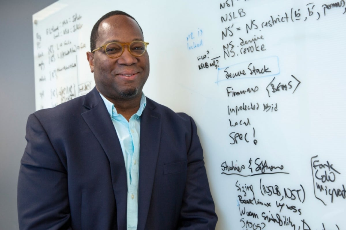 Portrait of ASU Associate Professor Michel Kinsy standing in front of a whiteboard in a classroom.