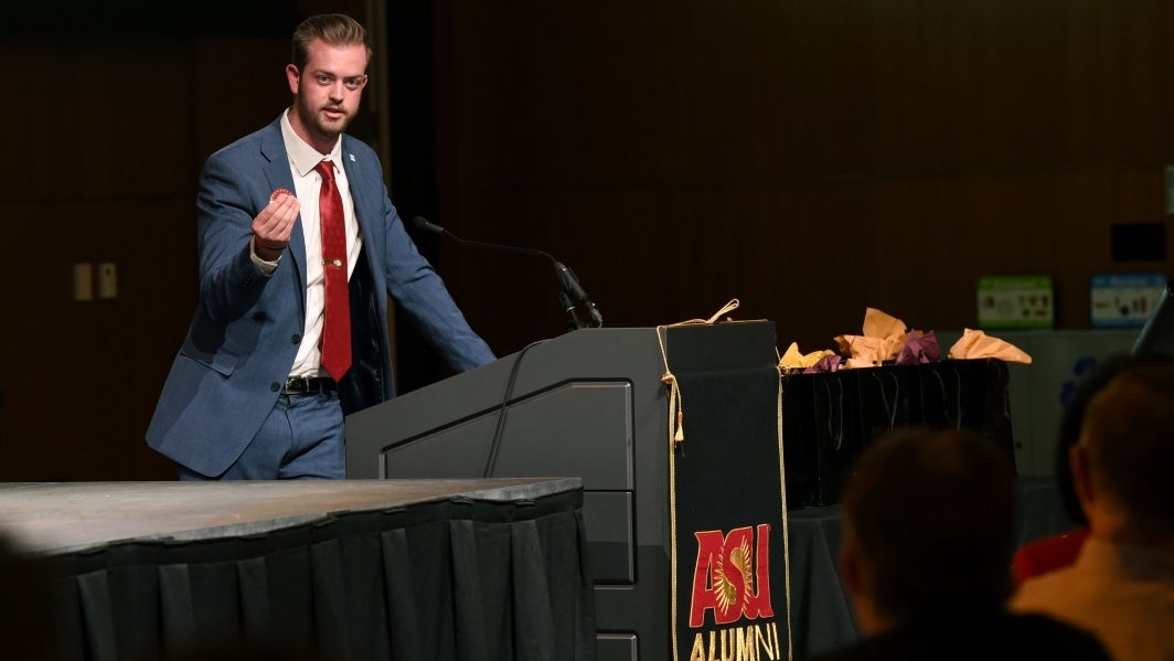 Man in a blue suit and red tie speaking behind a lectern.