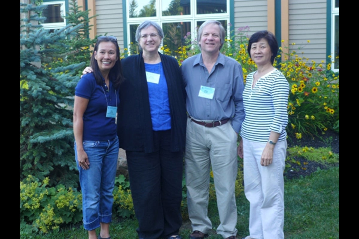 Four people posing for photo in front of house