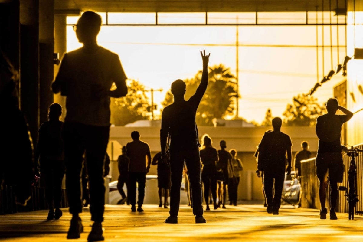 Silhouetted students walk down an outdoor hallway, including one in the middle holding his hand in a pitchfork gesture