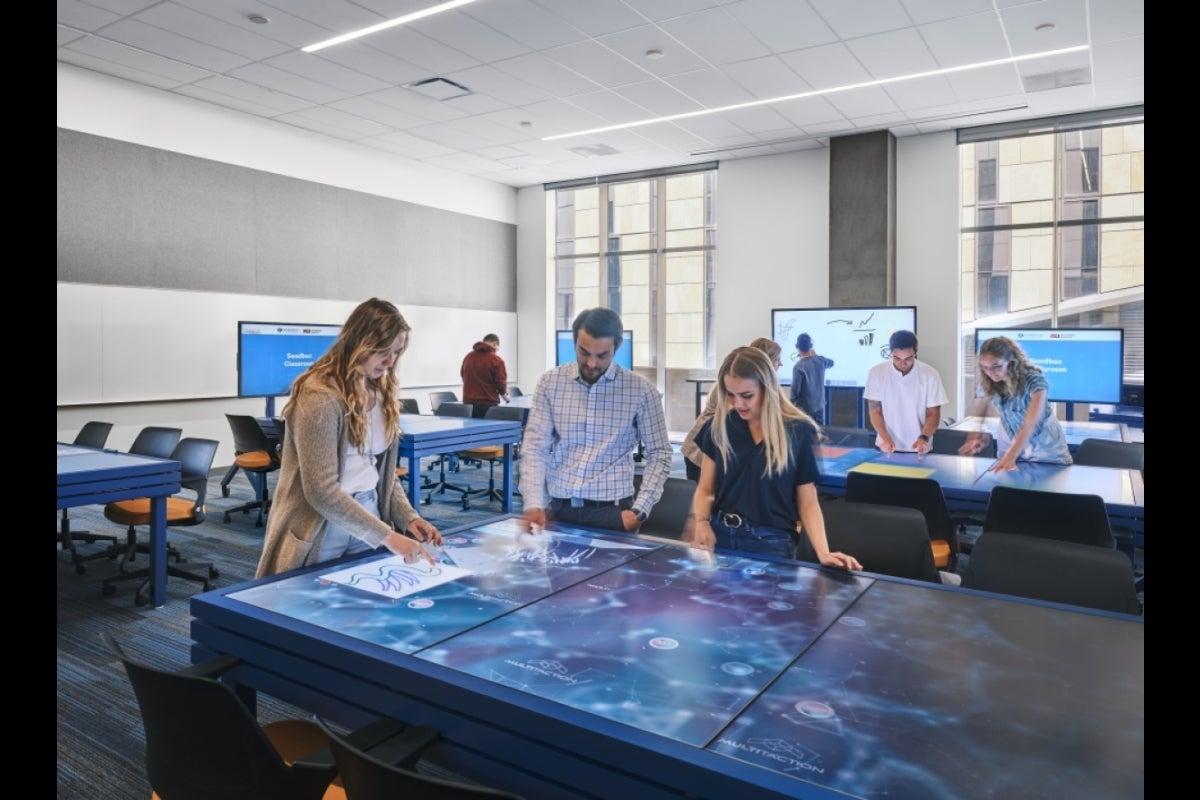 People standing around a table that uses technology to let them draw on it with their fingers.