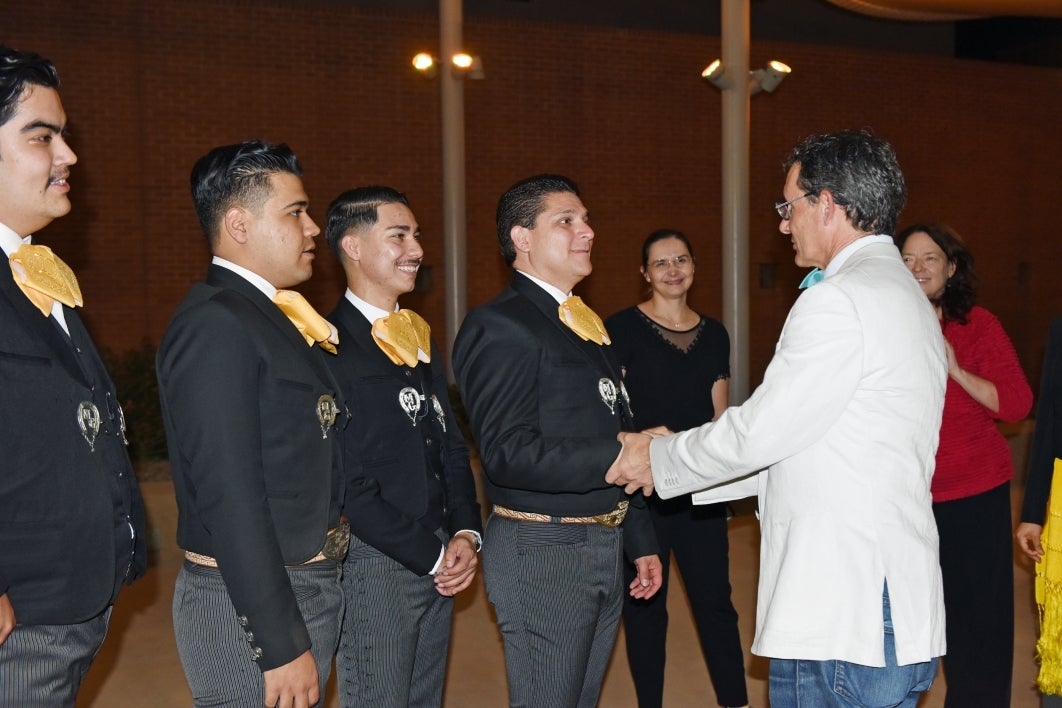 Man wearing a white suit jacket shaking the hands of mariachi band members.