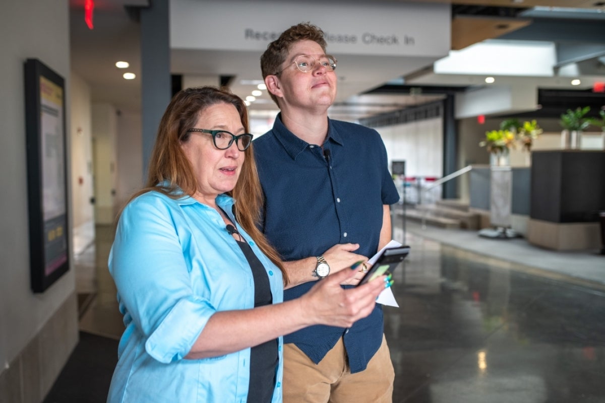 Two people looking out toward the horizon as one holds a device.