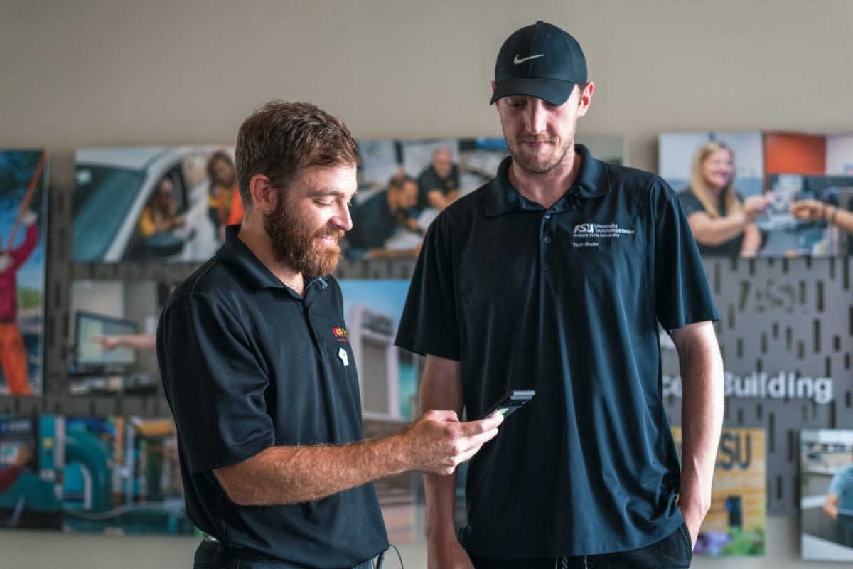 Two men smiling and looking at a device.