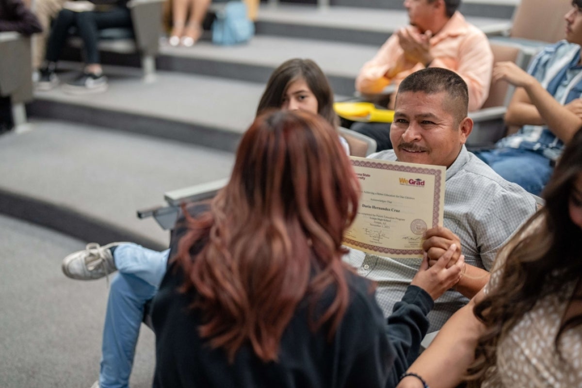 Man seated in an audience, smiling as he accepts a certificate.