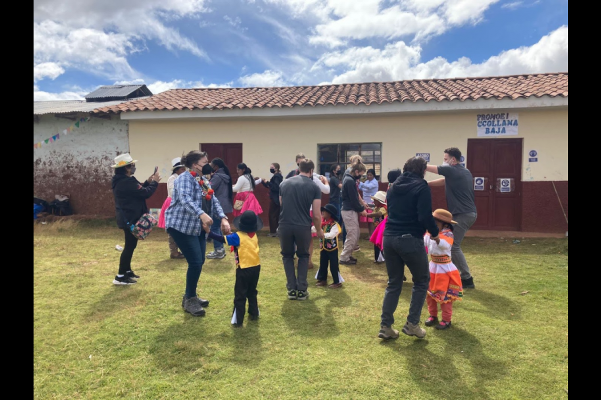 Students dance with local children in a community in Peru in the background is a community center