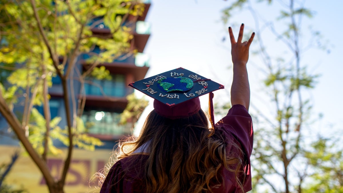 student in cap and gown giving pitchfork sign