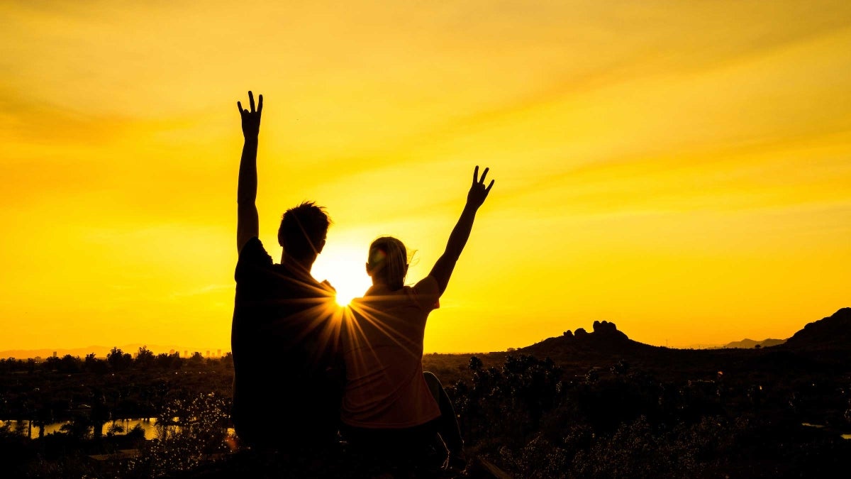 Silhouetted people hold up pitchfork gestures against a setting sun