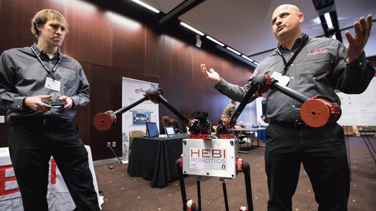 Men demonstrate a robot at a symposium