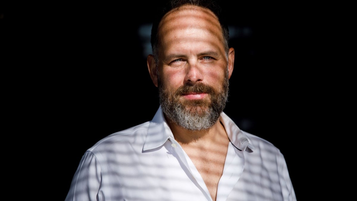 Gaymon Bennett wearing a white button up shirt is illuminated against a dark background.