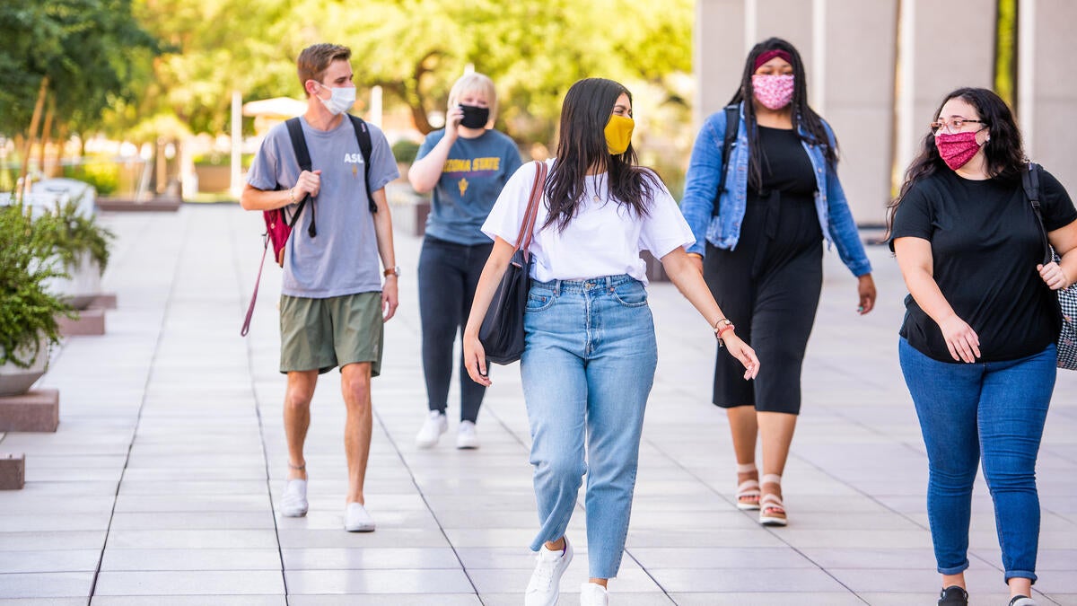 Students walk on a sidewalk while distancing and wearing face coverings