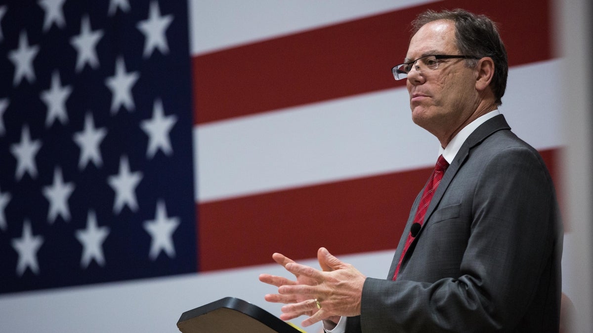 Man speaking at lectern with American flag behind him