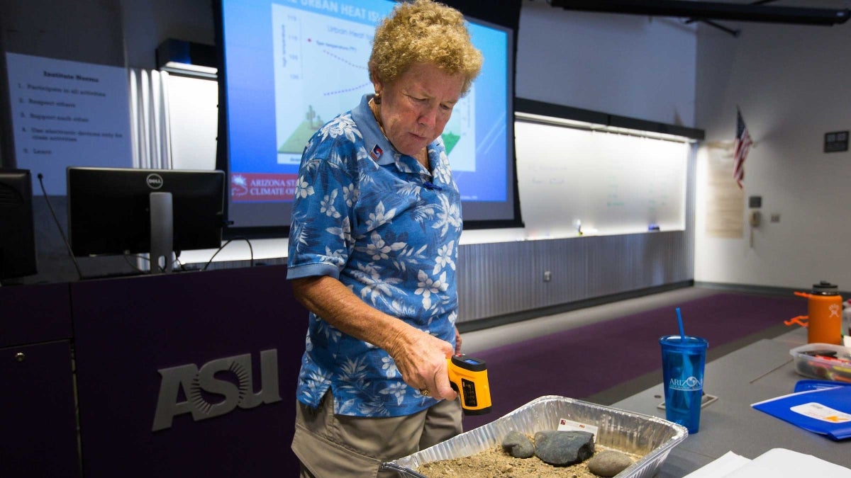 A woman points a thermometer at a pan of dirt and stones that had been outside for 90 minutes