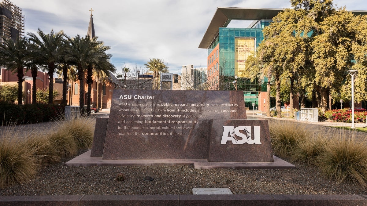 A sign showing the ASU charter with buildings behind it.