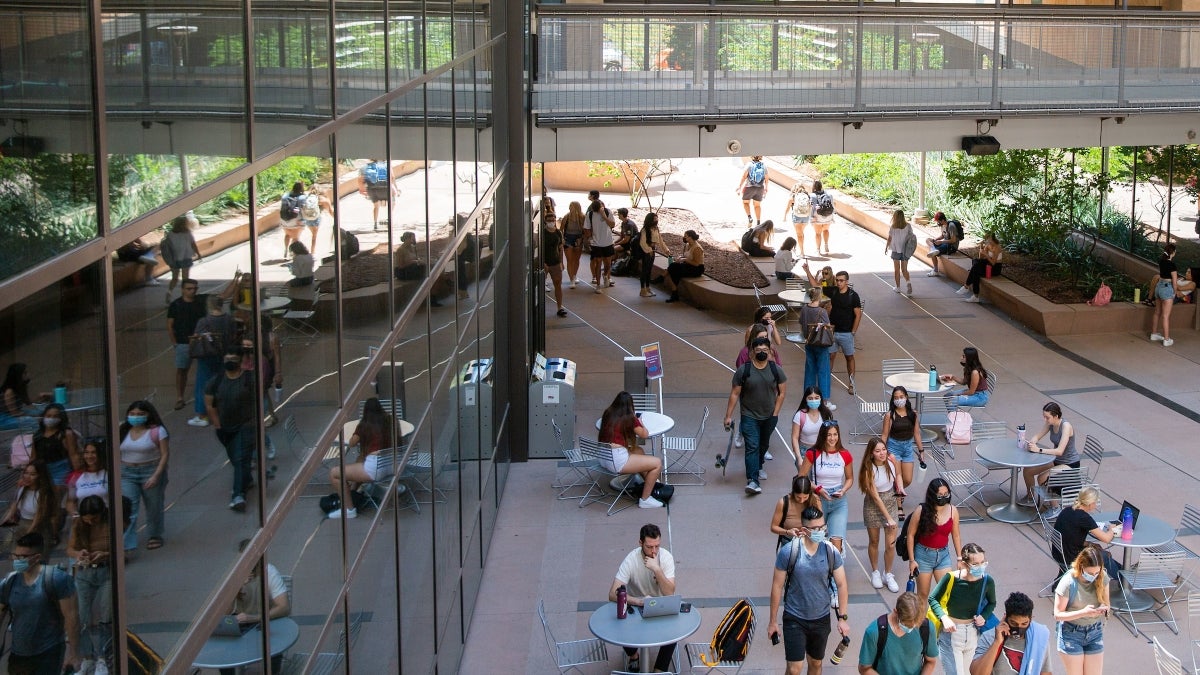 Students walk through a corridor between buildings while some sit at tables