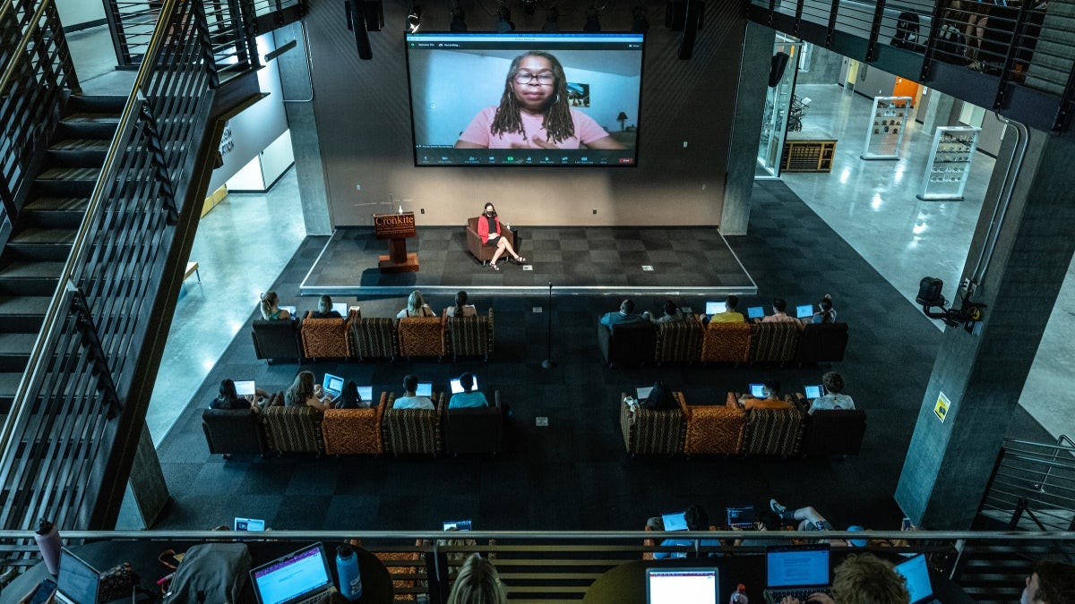 woman speaking to crowd via Zoom on overhead projector