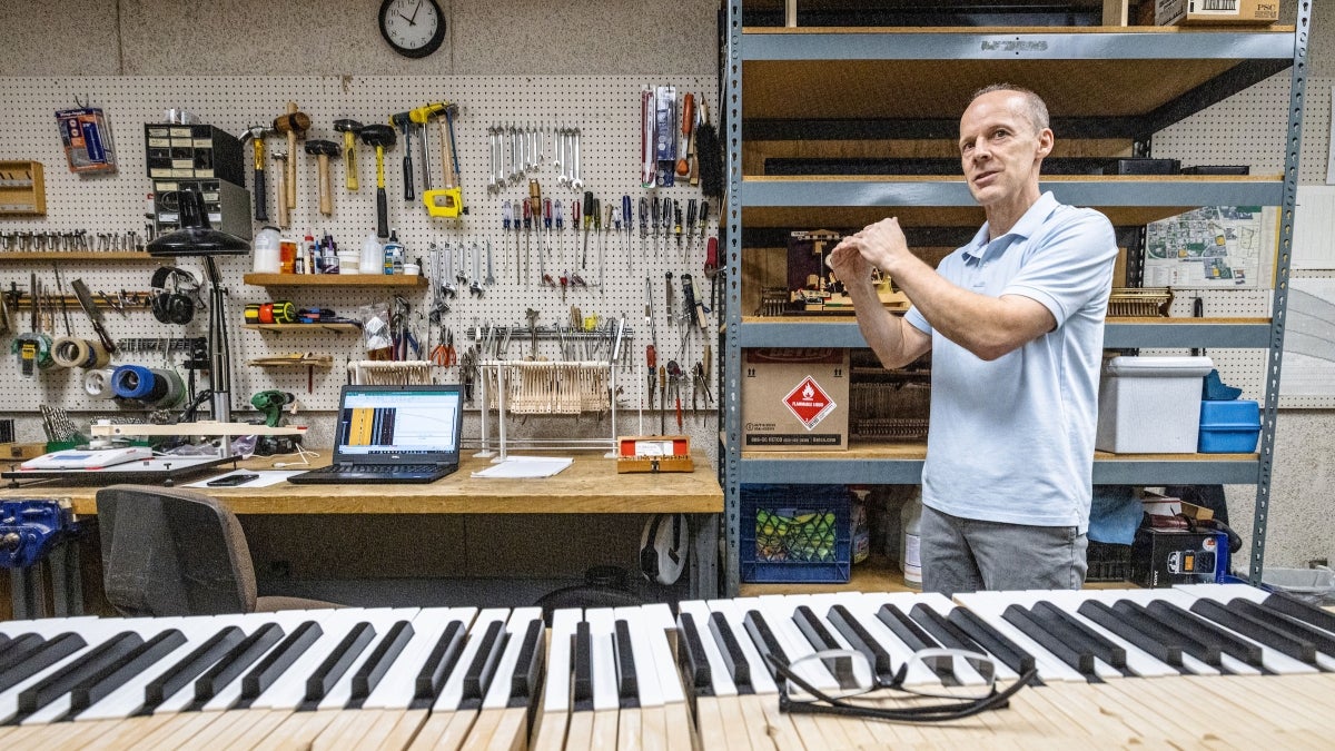 Man gesturing in piano workshop with piano keys laid out in front of him.