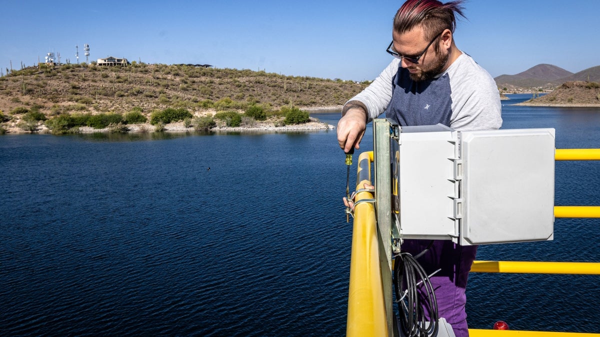 Man attaching a battery to a fence near a lake