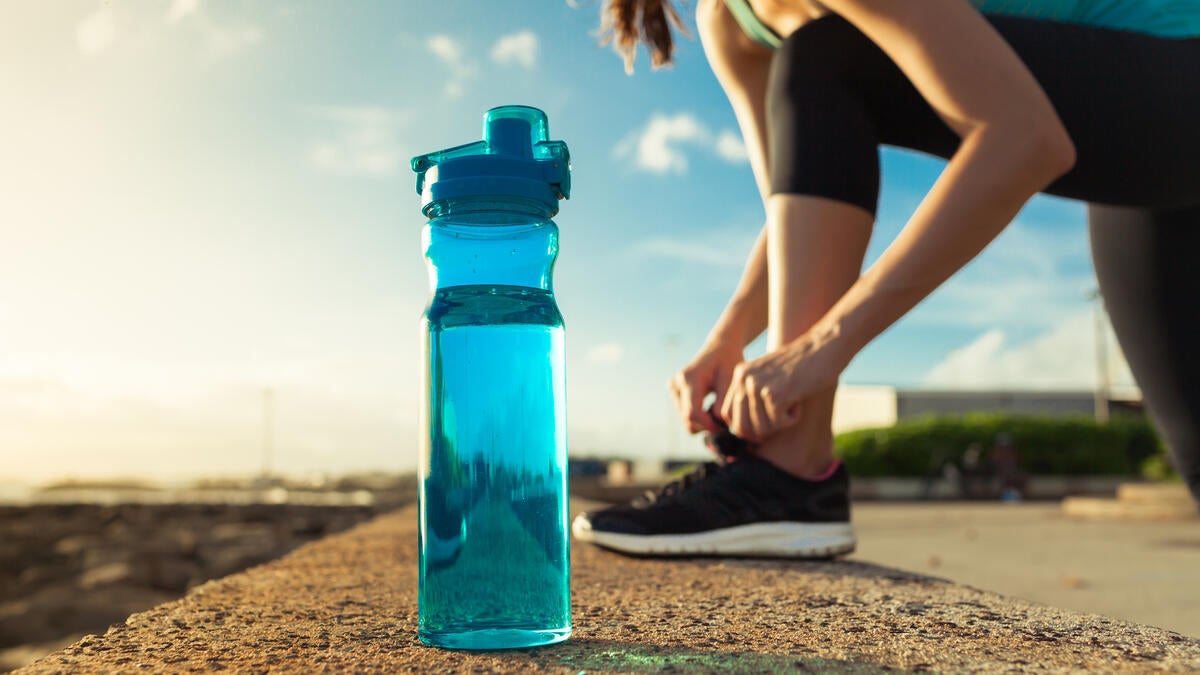 Person tying a shoe with a water bottle in the foreground.