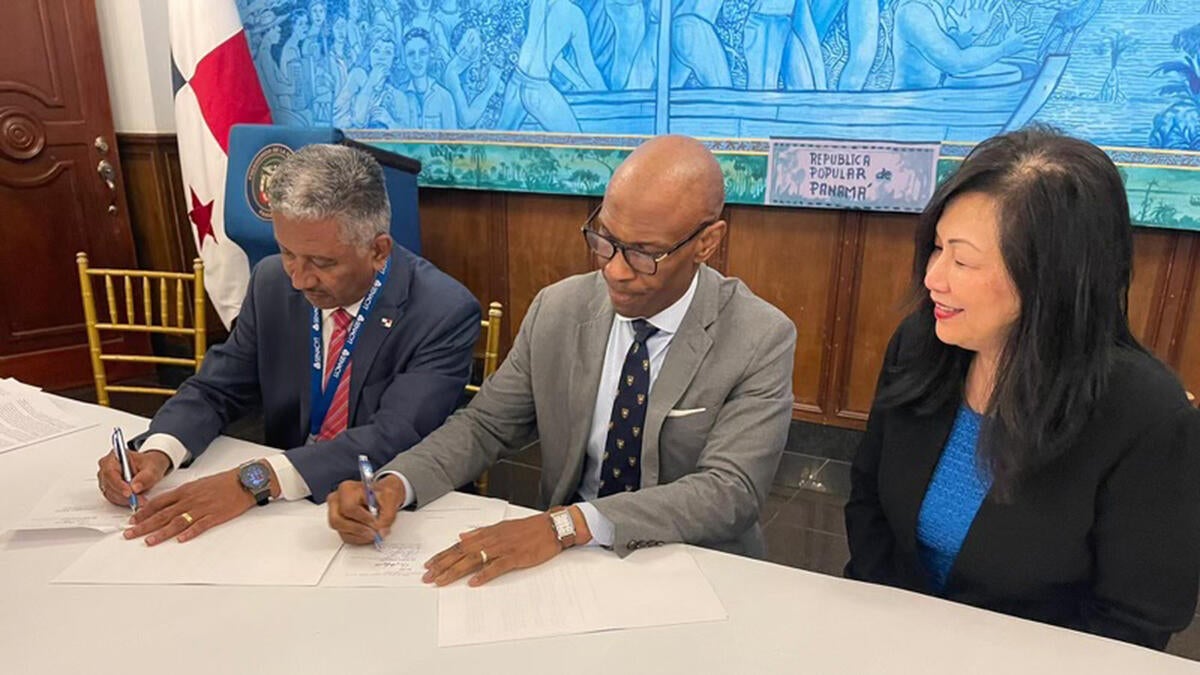 Three people sit at a table signing documents