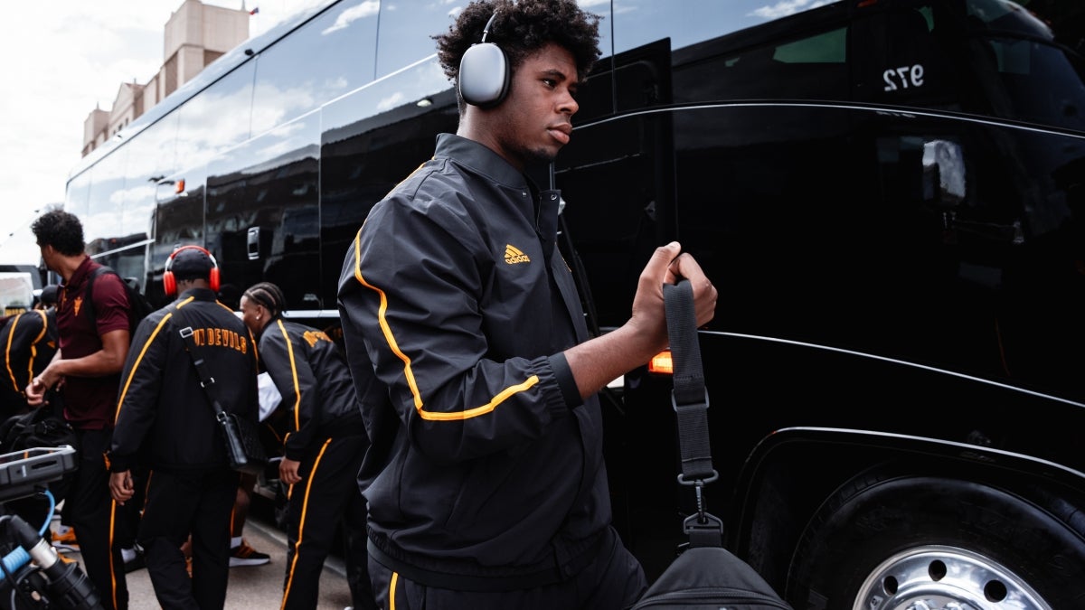 ASU football players in track suits board black charter buses