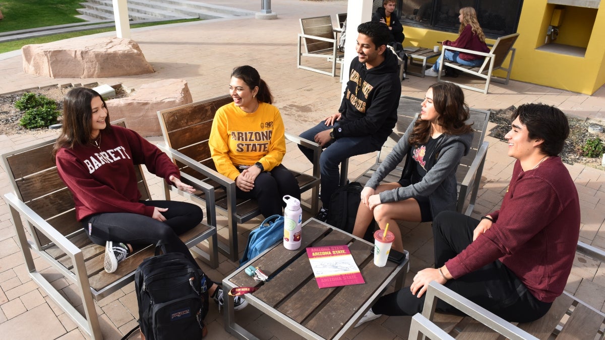 Students wearing Arizona State University clothing gathered in a circle talking.