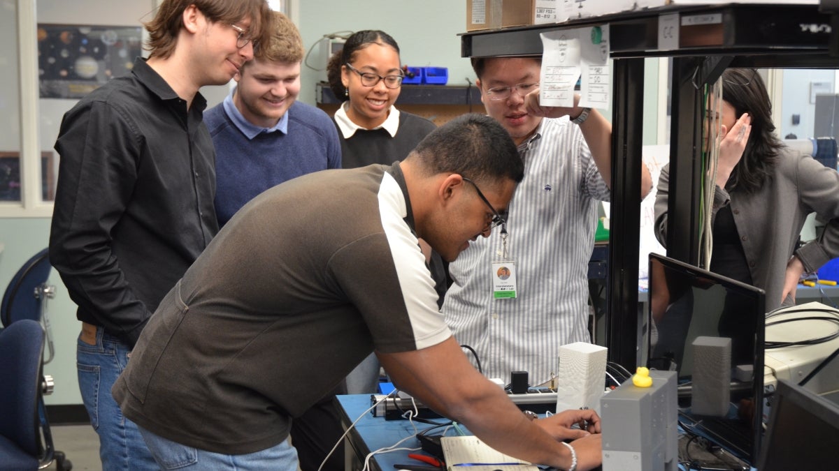 Man standing in front of something with group of students around him