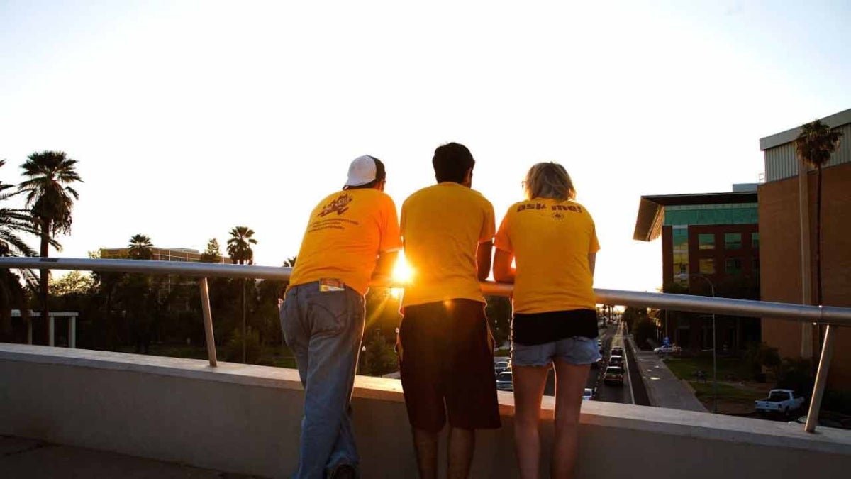 3 ASU students on a bridge look over University Drive as the sun sets