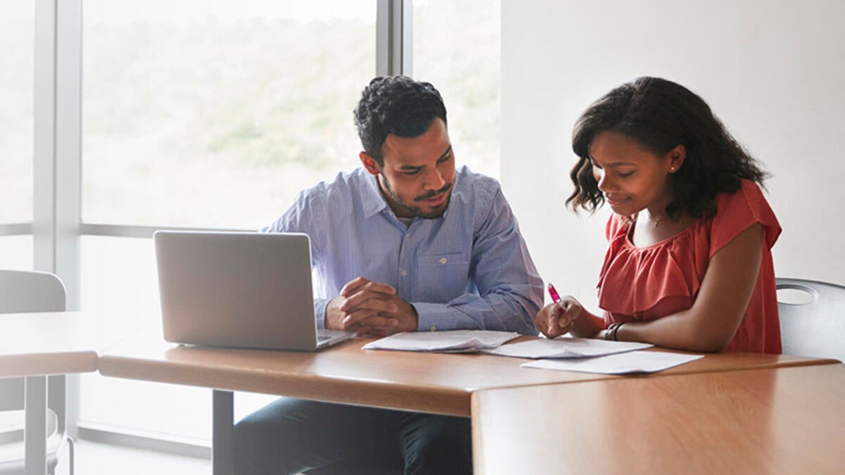 A woman and man in front of a laptop with papers on a desk