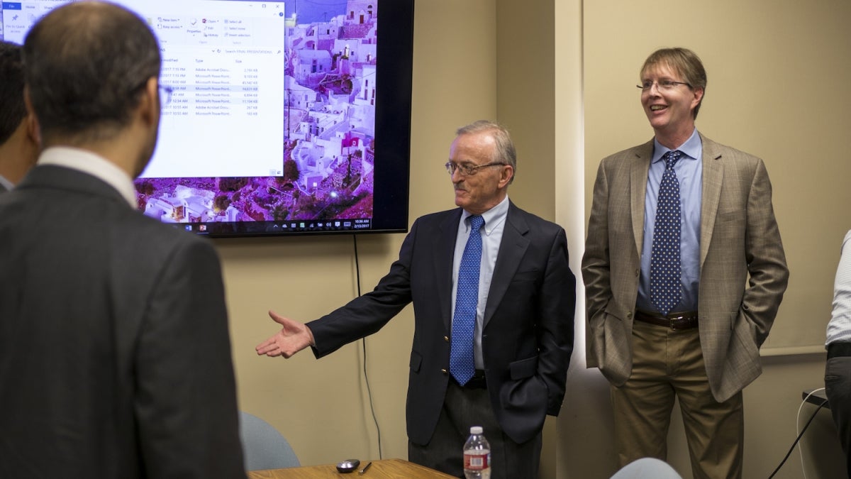 Photo of Constantine Balanis standing in front of a monitor with his right arm outstretched with a caption of "Constantine Balanis (center) along with a team of researchers from Arizona State University and the King Abdulaziz City for Science and Technolo