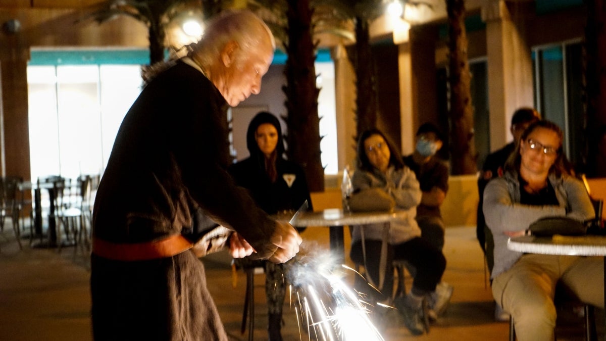 Man demonstrating tools from the Iron Age. Sparks fly from the tool as students look on.