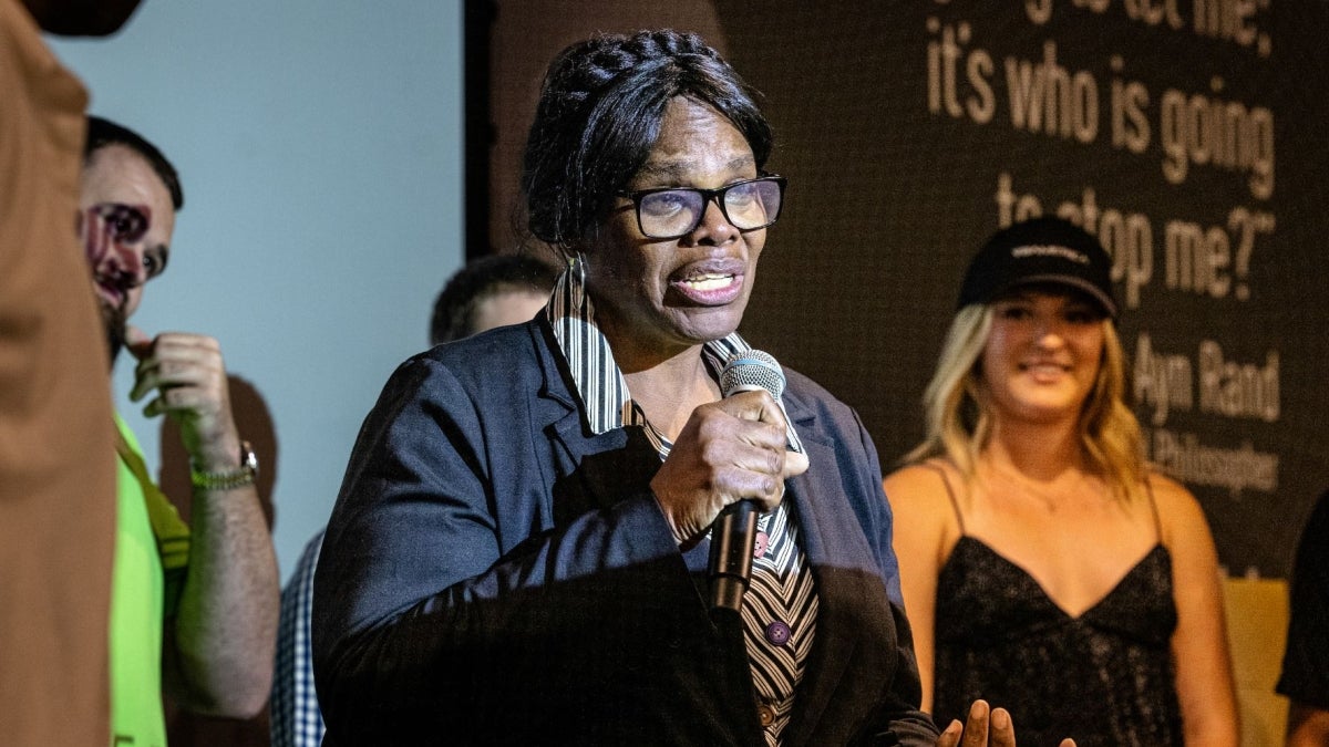 Woman standing on stage speaking into microphone.