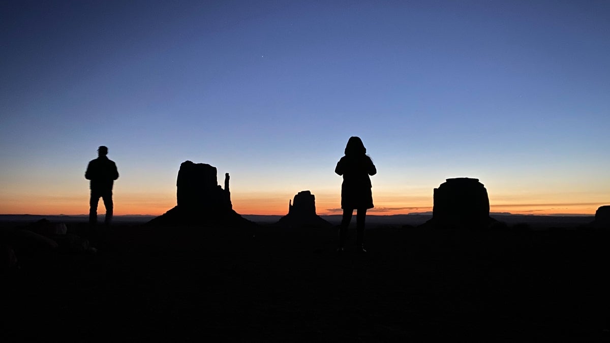 Two people silhouetted against a backdrop of desert scenery.