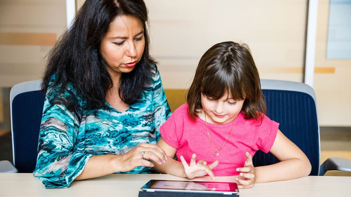 woman shows young girl EMBRACE app on tablet