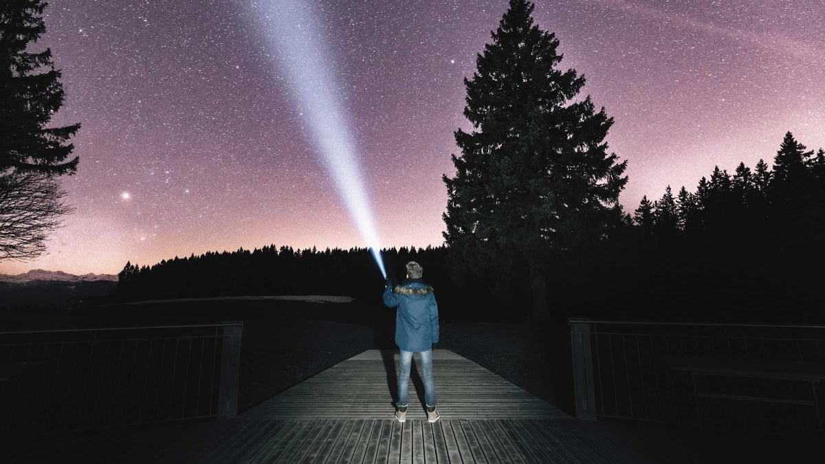 photo of man shining flashlight at starry sky