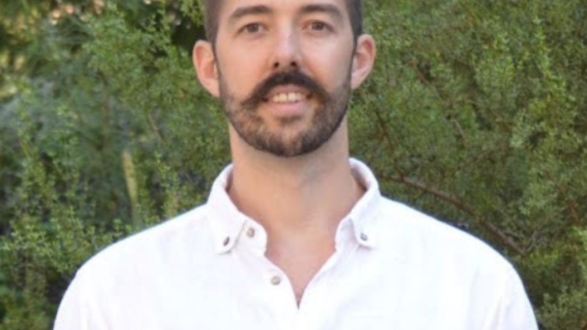 Portrait headshot of Assistant Professor Nathan Upham with greenery behind him.