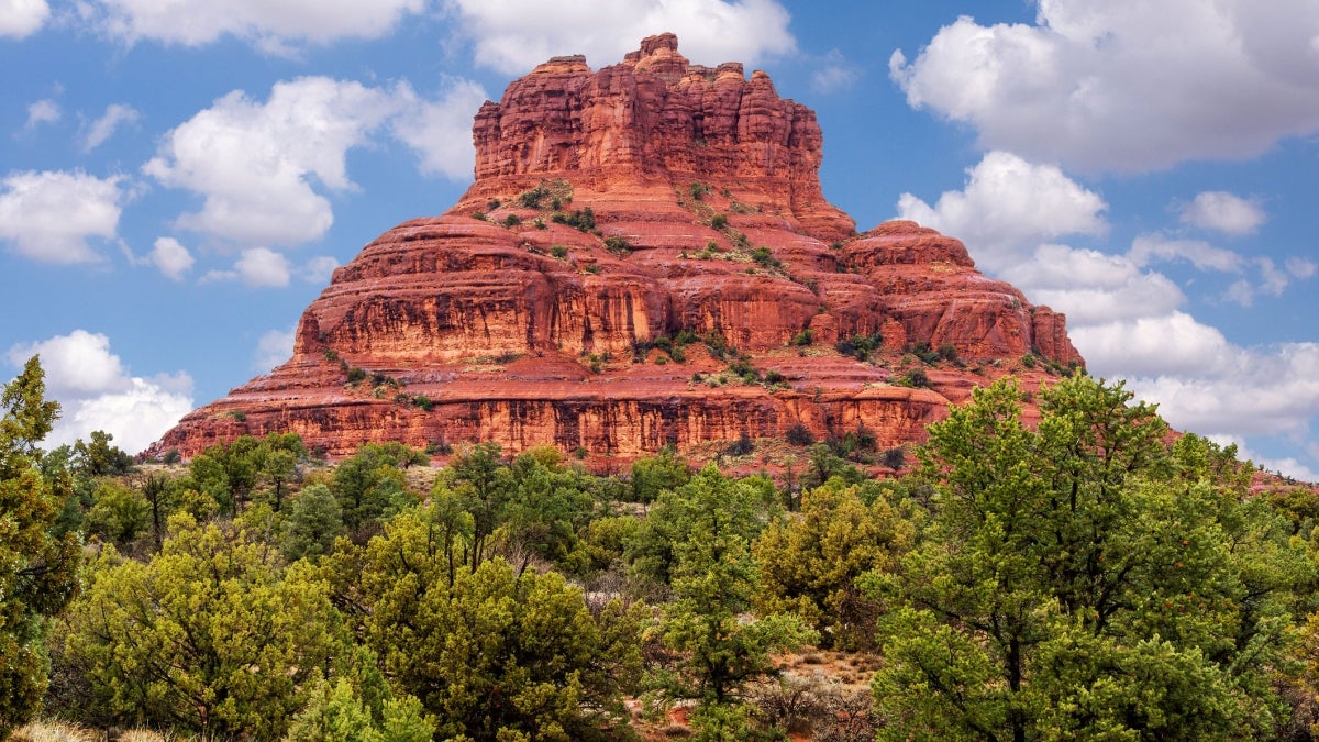 A red rock mountain rises above green trees in Sedona